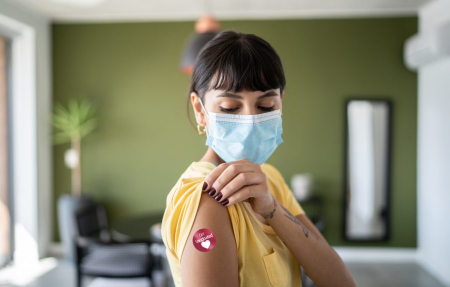 La mujer joven que usaba la mascarilla protectora que demostraba el brazo con “consiguió” la etiqueta engomada vacunada encendido en MD Now
